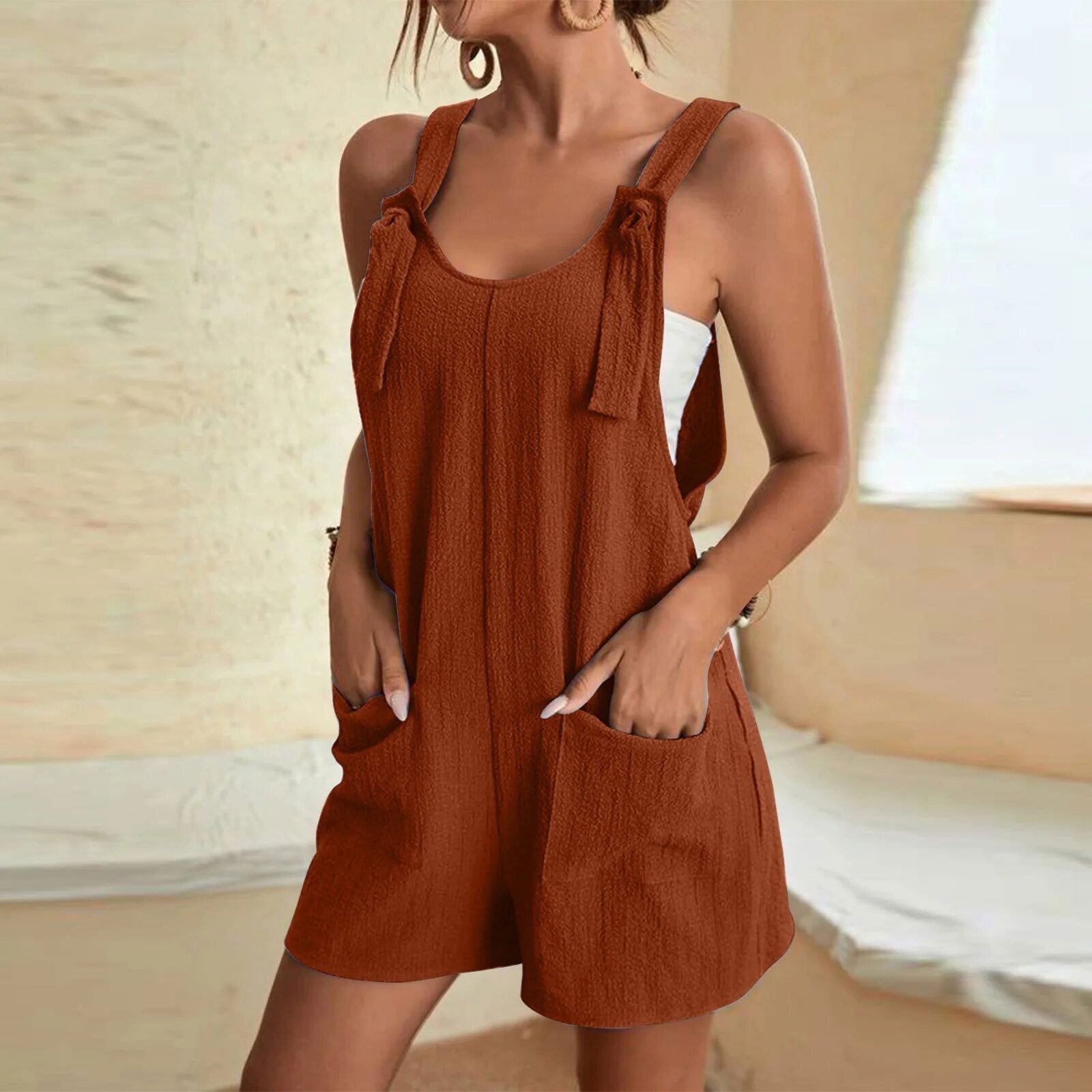 Donna in salopette corta marrone, tessuto leggero, con tasche frontali. Abbigliamento estivo casual, moda femminile, stile rilassato.