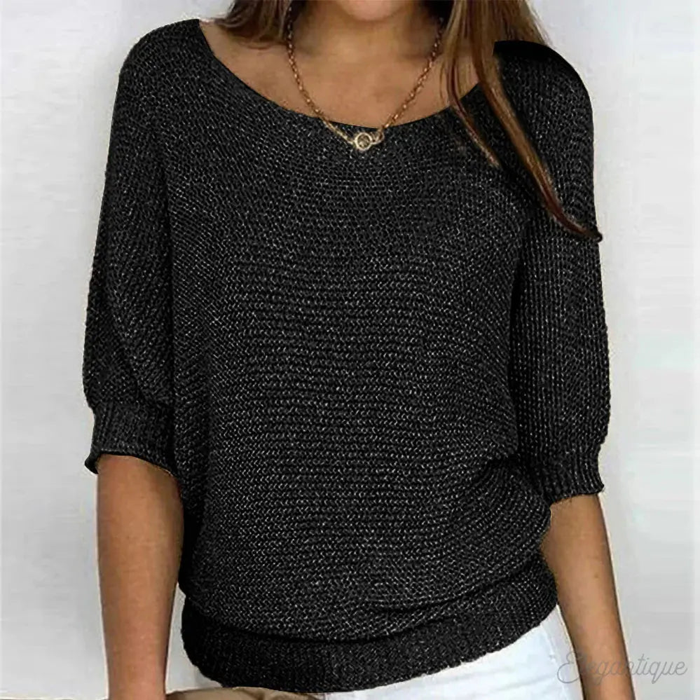 Maglia nera a maniche corte, tessuto lavorato a maglia, scollo a barca, indossata con pantaloni bianchi. Elegante e casual per moda donna.