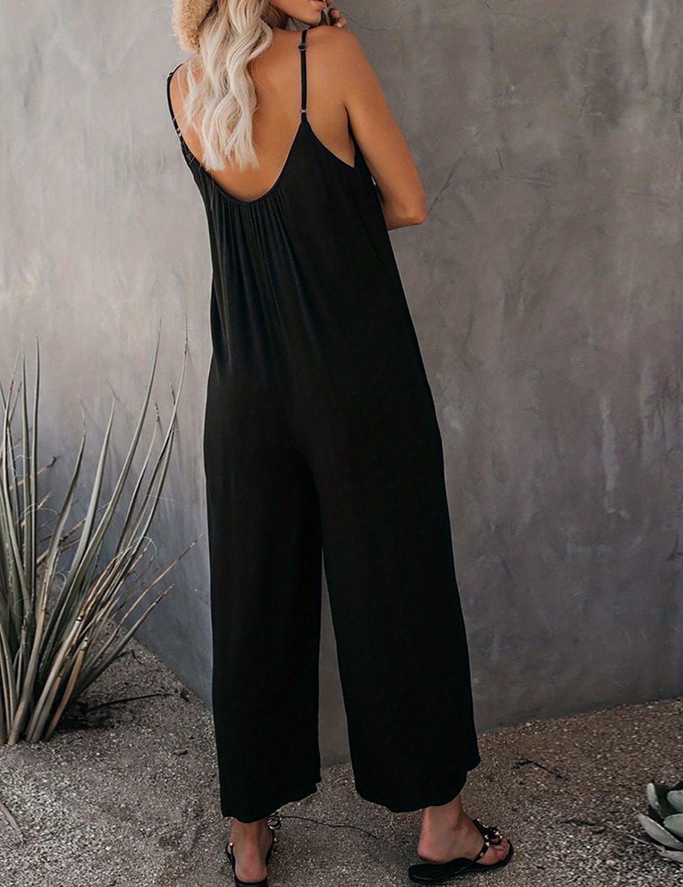 Donna in tuta nera estiva, spalline sottili, schiena scoperta, sandali neri, sfondo grigio. Moda casual elegante, abbigliamento donna estivo.