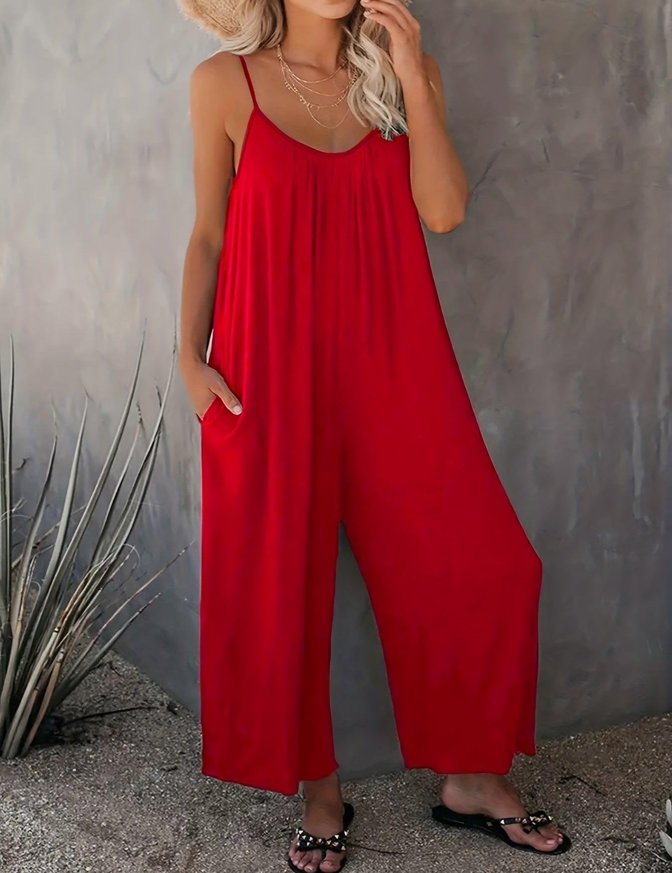 Donna con tuta rossa estiva, spalline sottili, sandali neri, sfondo grigio. Moda femminile, abbigliamento casual elegante, tendenza estiva.