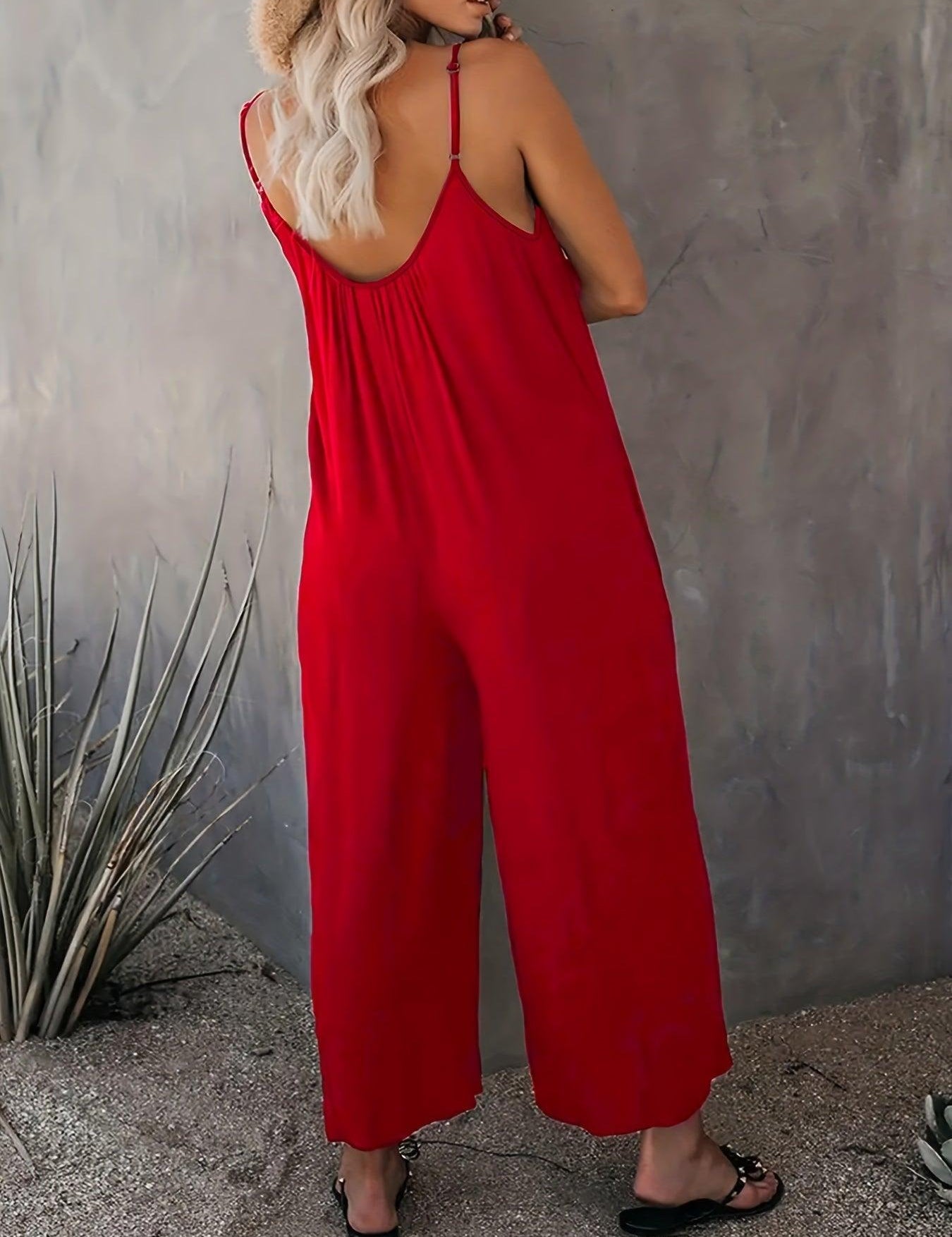 Donna in tuta rossa estiva, spalline sottili, sfondo grigio, piante decorative. Moda femminile, abbigliamento casual elegante.