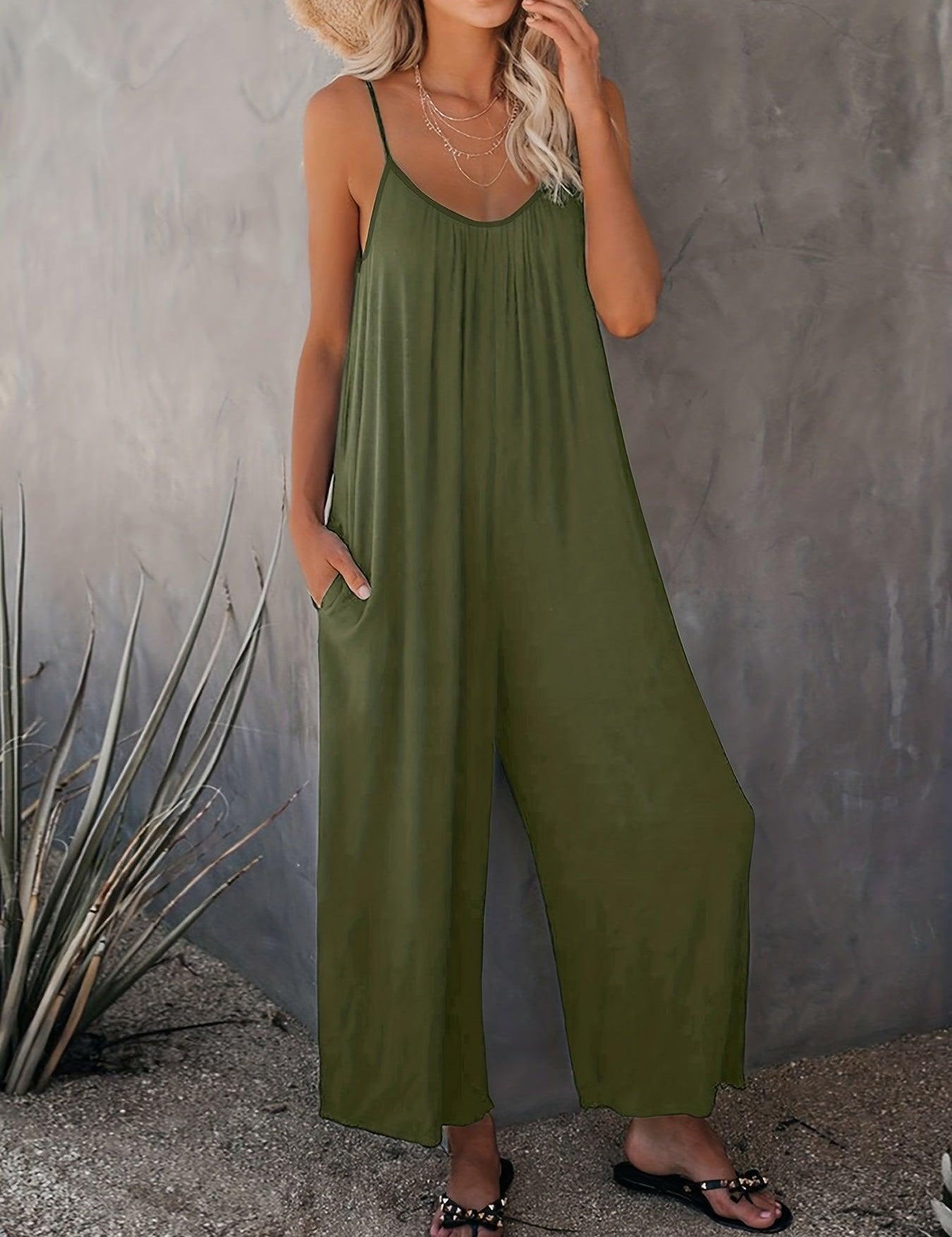 Donna con tuta verde oliva estiva, spalline sottili, sandali neri, cappello di paglia, sfondo grigio. Moda casual, abbigliamento estivo elegante.