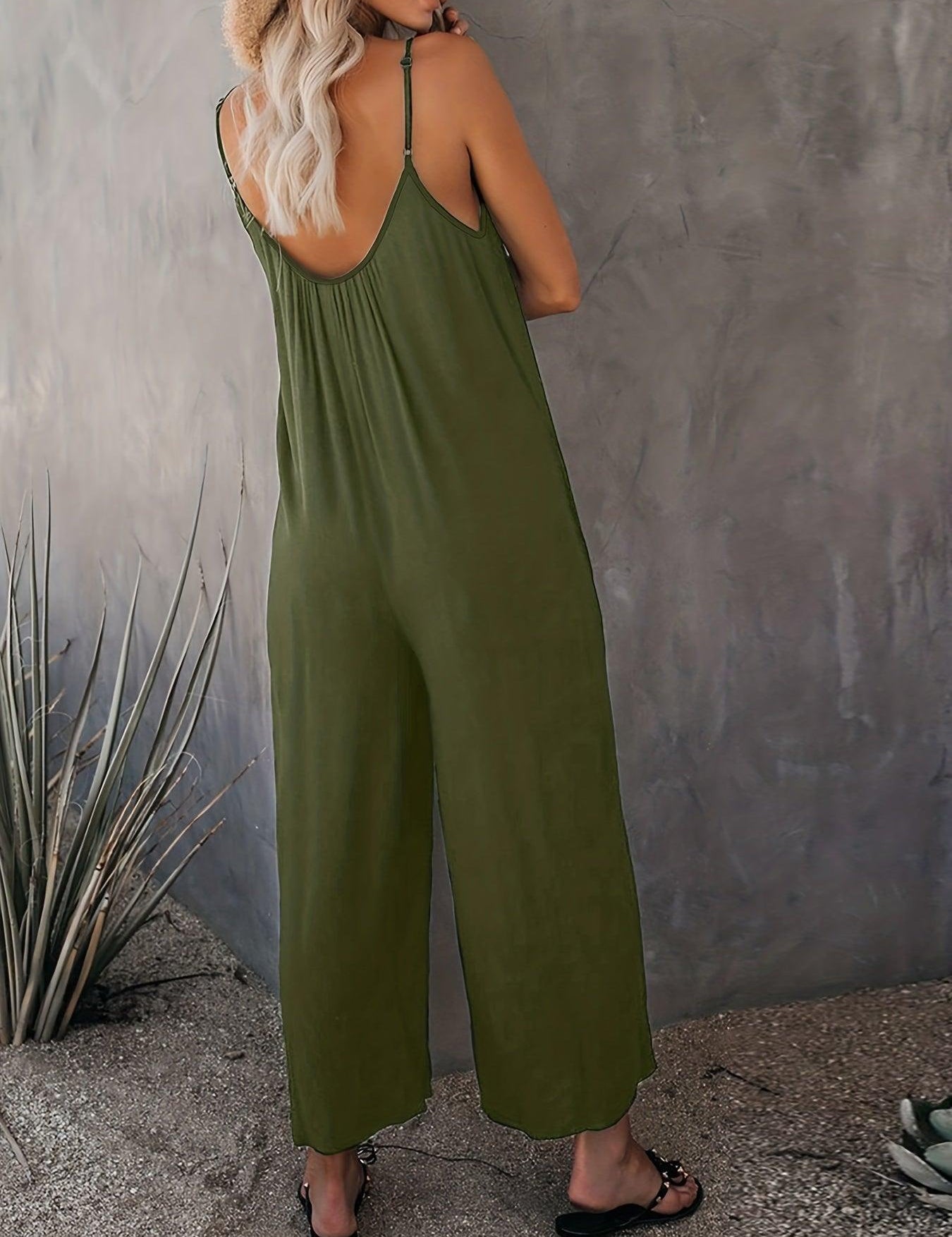 Donna con tuta verde oliva senza maniche, sandali neri, cappello di paglia, sfondo grigio. Moda estiva casual, abbigliamento femminile trendy.