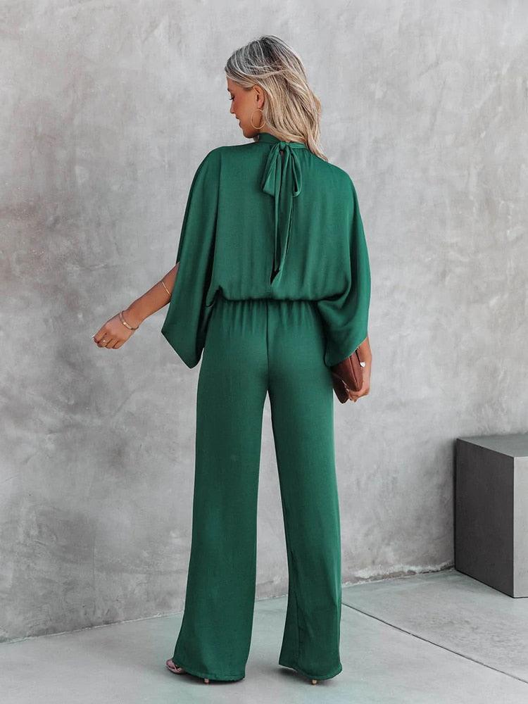 Donna in tuta verde elegante, maniche ampie, sfondo grigio. Moda femminile, abbigliamento casual chic, tendenza 2023.