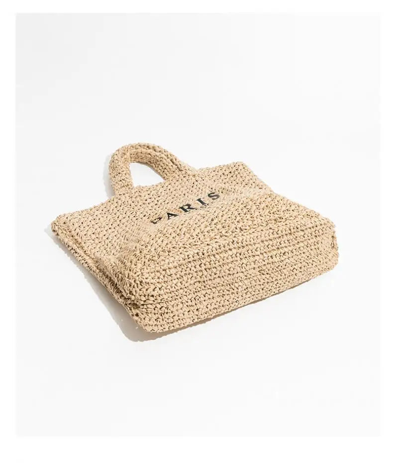 Borsa tote in paglia beige con manici intrecciati e scritta "Paris" nera, ideale per shopping estivo e look casual chic.