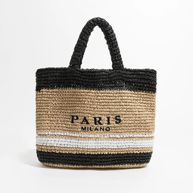 Borsa tote in paglia intrecciata con manici neri, scritta "Paris Milano" e strisce nere e bianche. Accessorio moda estivo elegante.