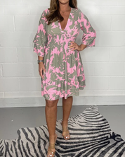 Abito donna floreale rosa e verde, maniche a tre quarti, scollo a V, lunghezza al ginocchio, indossato con sandali beige su tappeto zebrato.
