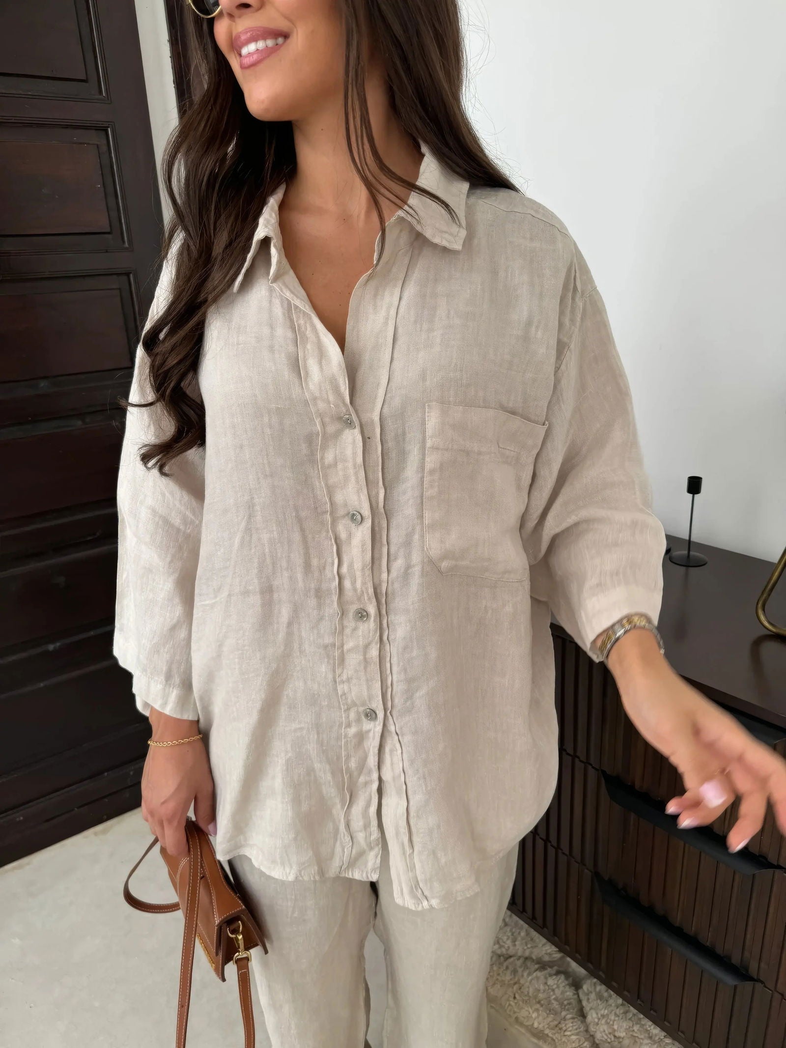 Donna con camicia di lino beige, maniche lunghe, tasca frontale, abbinata a pantaloni coordinati. Look casual ed elegante, moda donna 2023.