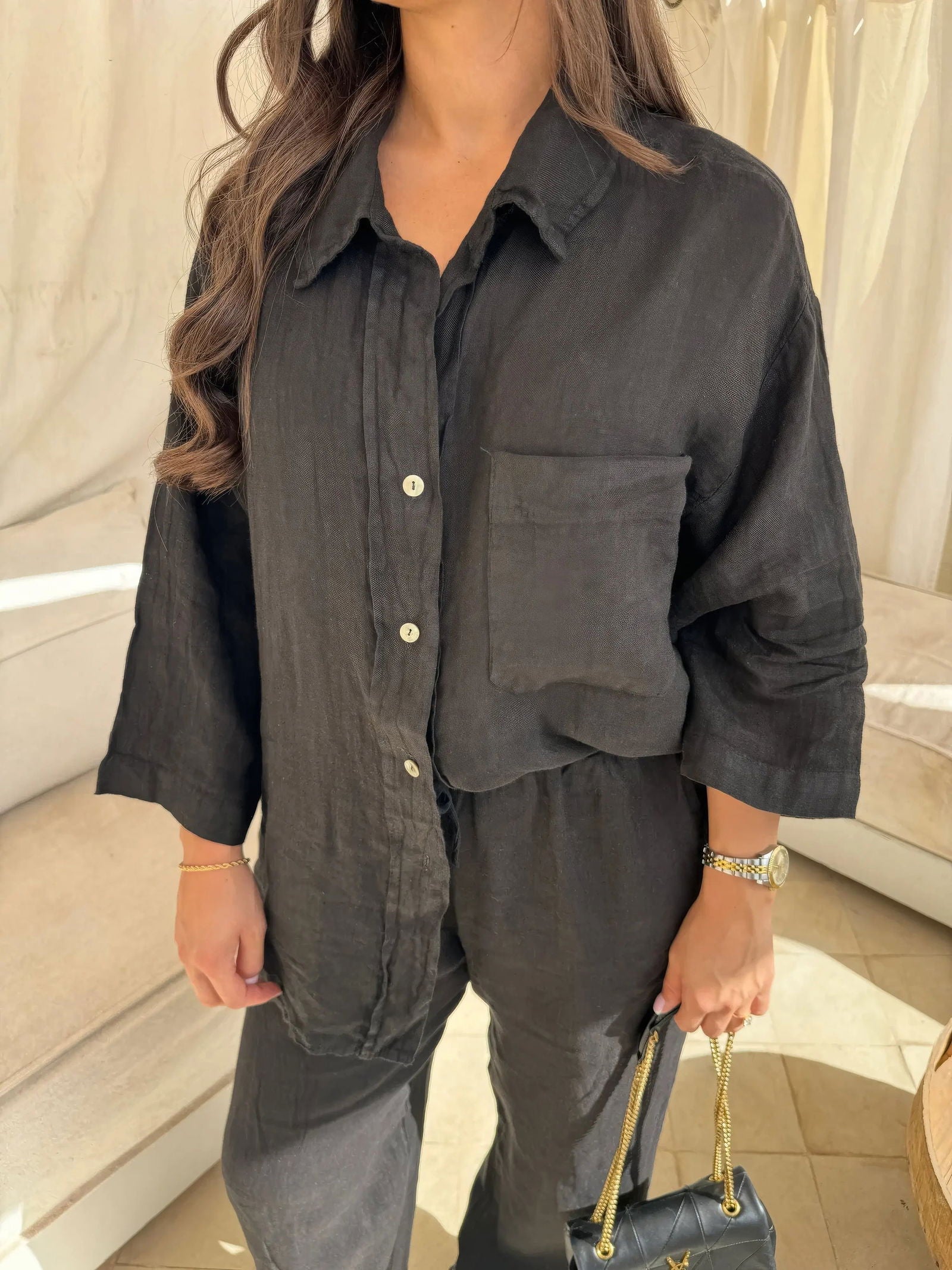 Donna con camicia nera di lino, maniche lunghe, tasca frontale, abbinata a pantaloni coordinati. Moda casual elegante, outfit estivo.