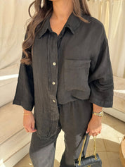Donna con camicia nera di lino, maniche lunghe, tasca frontale, abbinata a pantaloni coordinati. Moda casual elegante, outfit estivo.