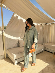 Donna con abito coordinato verde, occhiali da sole e borsa arancione in un'area lounge all'aperto. Moda estiva, stile casual chic.