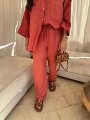 Donna in completo lino rosso, camicia e pantaloni, con sandali marroni e borsa a tracolla. Moda estiva, abbigliamento casual elegante.