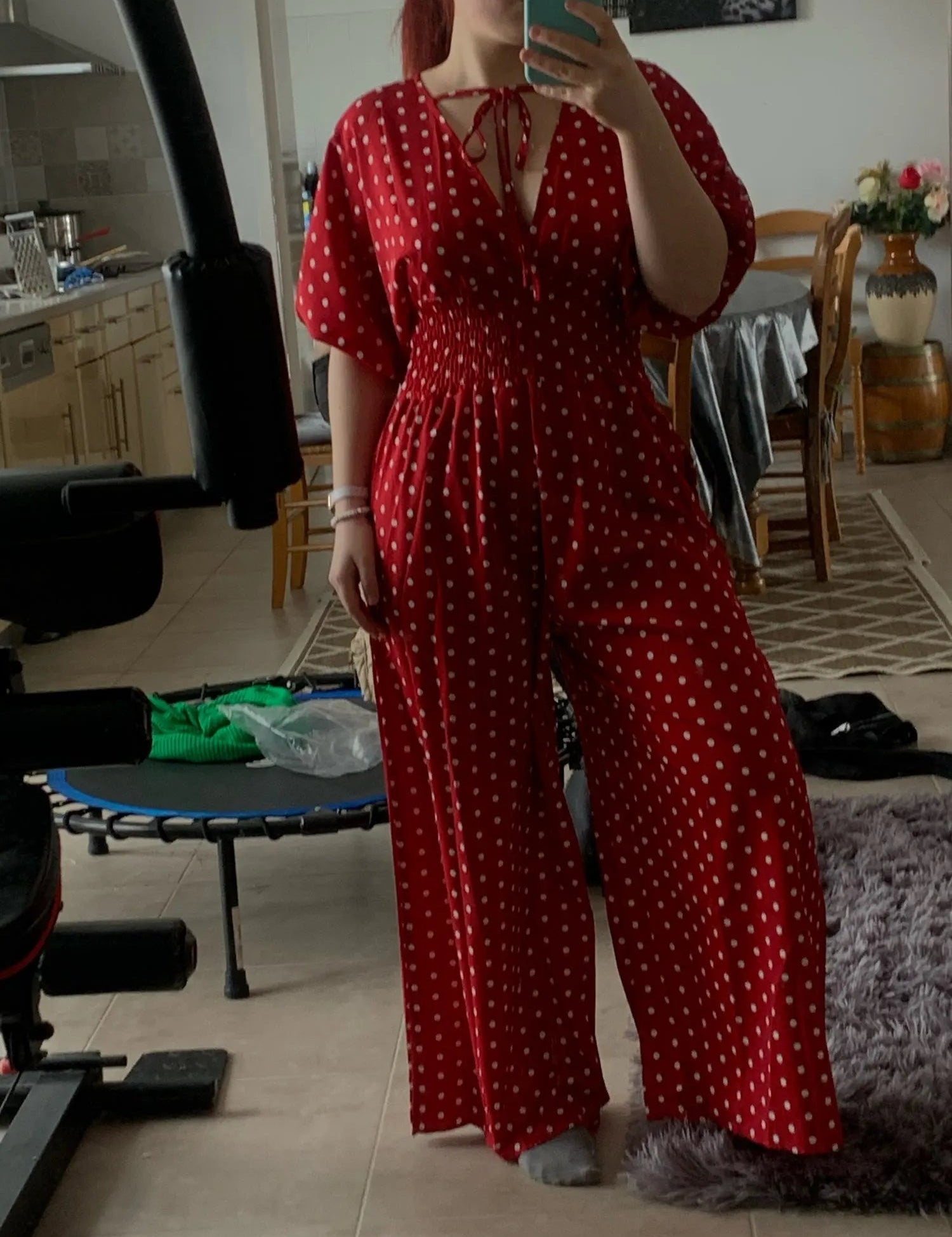 Donna in tuta rossa a pois bianchi, scollo a V, maniche corte, in una cucina moderna. Abbigliamento estivo elegante, moda femminile casual.
