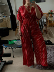 Donna in tuta rossa a pois bianchi, scollo a V, maniche corte, in una cucina moderna. Abbigliamento estivo elegante, moda femminile casual.
