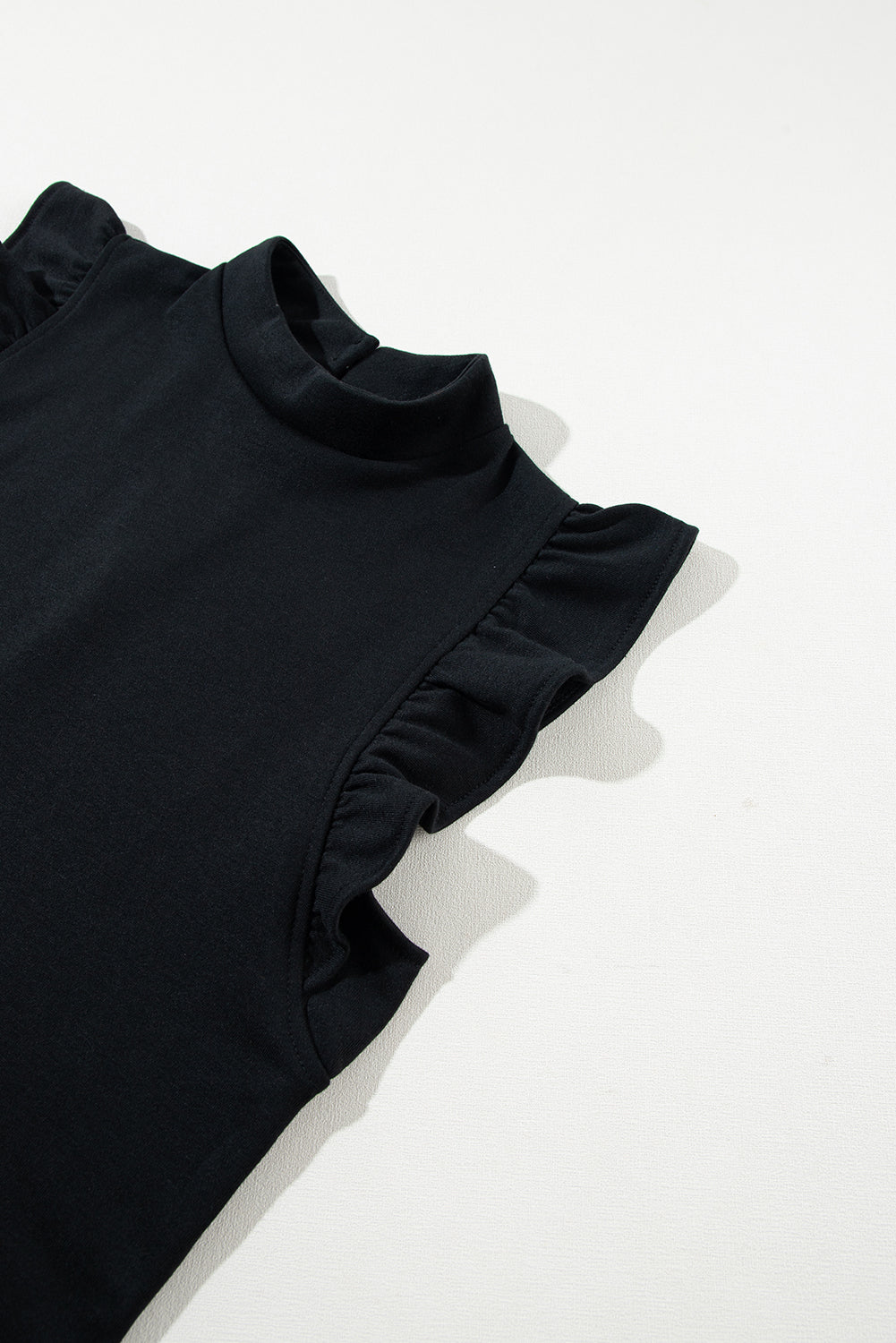 Maglia nera senza maniche con volant, collo alto, tessuto morbido. Elegante e versatile, ideale per look casual o formali.