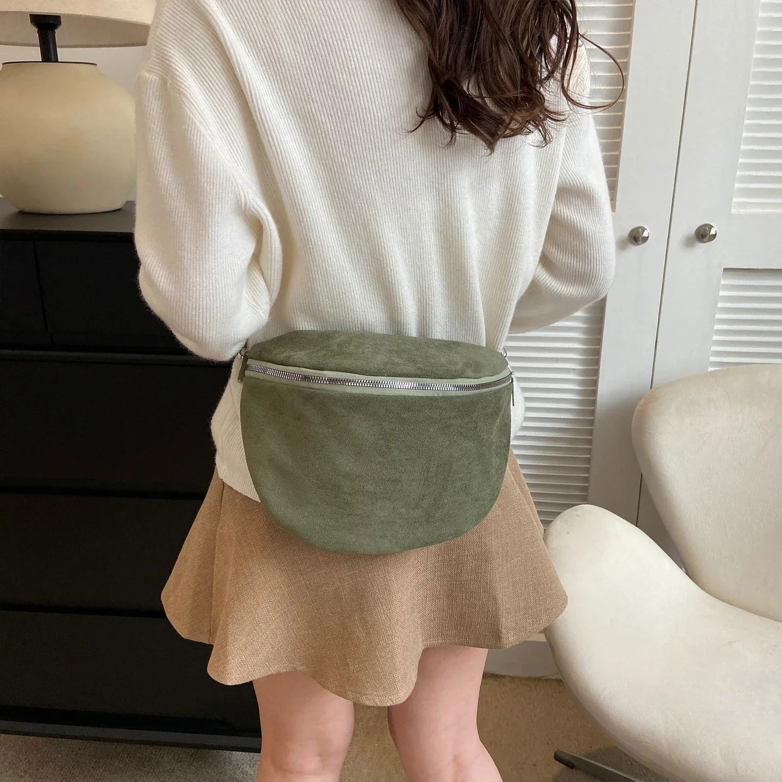Donna con marsupio verde oliva in tessuto scamosciato, indossa maglione bianco e gonna beige. Accessorio moda casual, stile urbano chic.