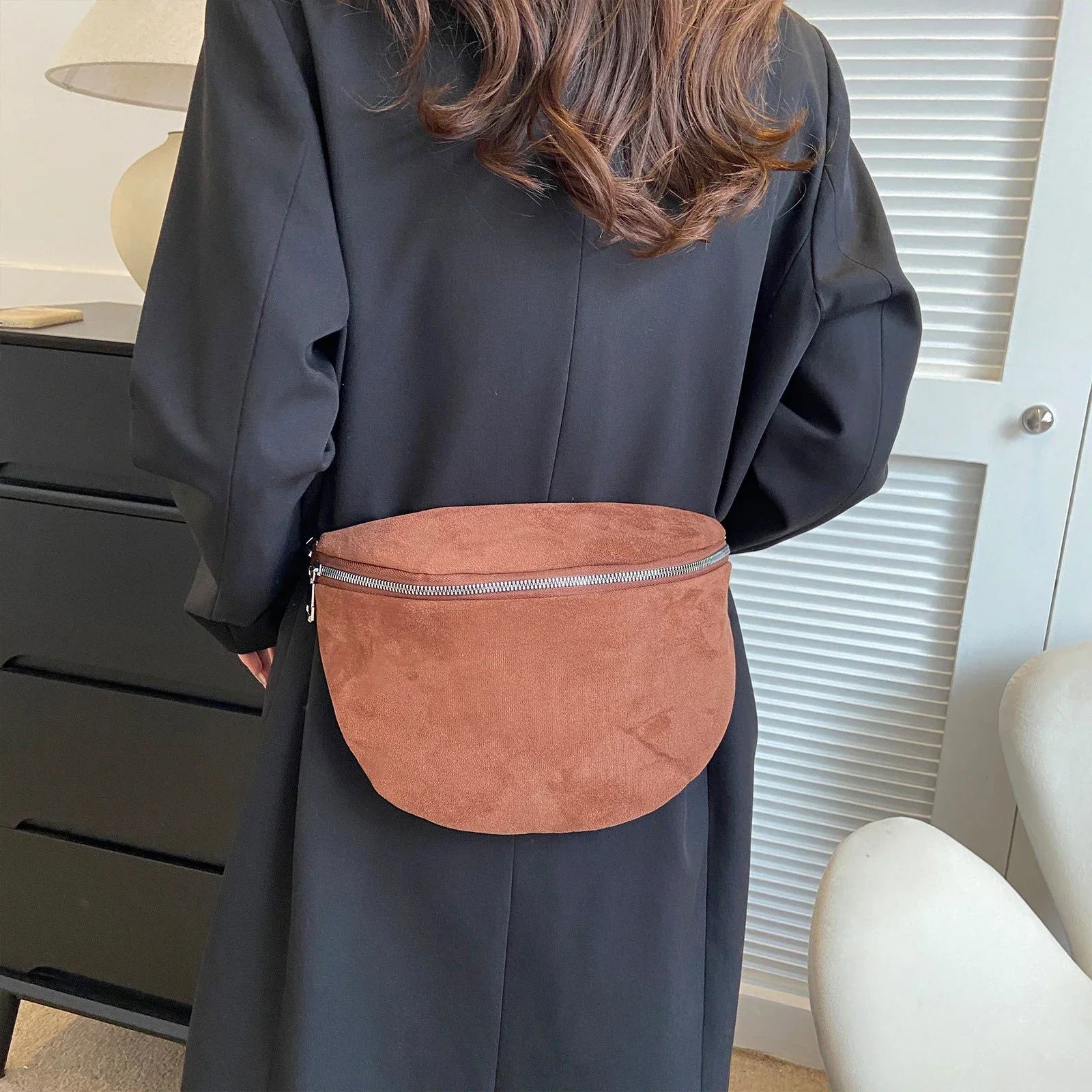 Donna con marsupio in pelle scamosciata marrone, indossa cappotto nero. Accessorio moda casual, chiusura con zip, ideale per look autunnali.
