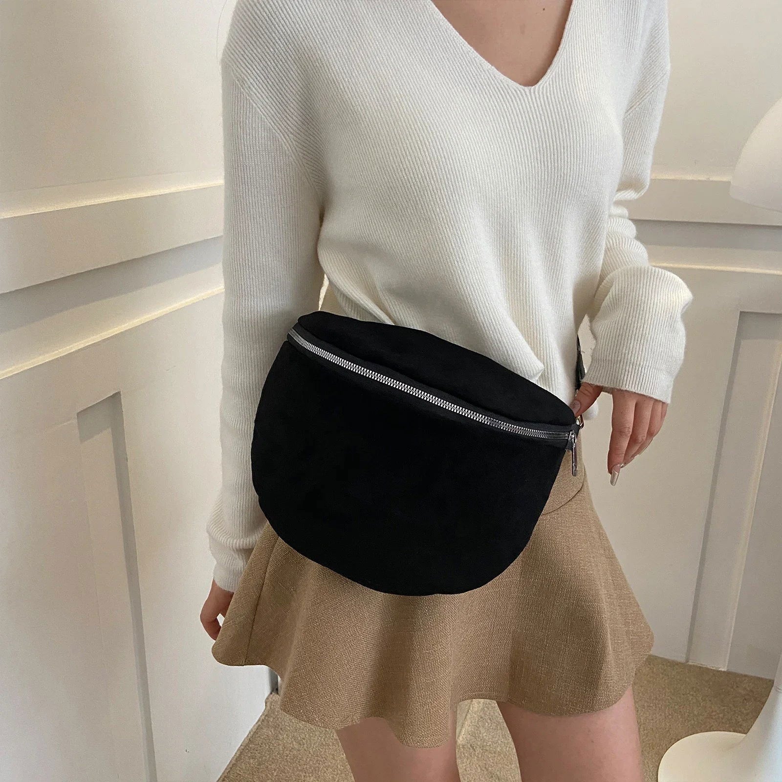 Donna con maglione bianco e gonna beige indossa marsupio nero elegante. Accessorio moda casual, perfetto per look autunnali e primaverili.