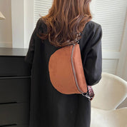 Donna con cappotto nero indossa borsa a tracolla marrone in pelle scamosciata, con cerniera e tracolla regolabile. Accessorio moda elegante e pratico.