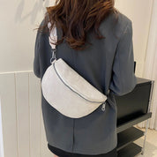 Donna con giacca grigia indossa marsupio bianco in pelle scamosciata, chiusura zip, tracolla regolabile. Accessorio moda casual elegante.