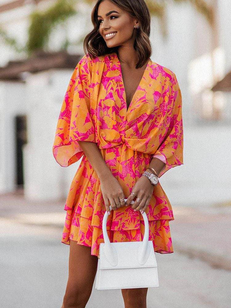 Donna sorridente con abito estivo floreale arancione e rosa, maniche ampie, e borsa bianca. Moda femminile, abbigliamento estivo elegante.