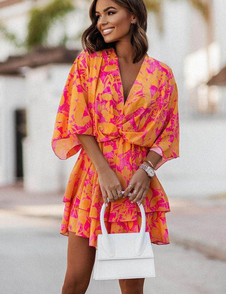 Donna sorridente con abito estivo floreale arancione e rosa, maniche ampie, e borsa bianca. Moda femminile, abbigliamento estivo elegante.