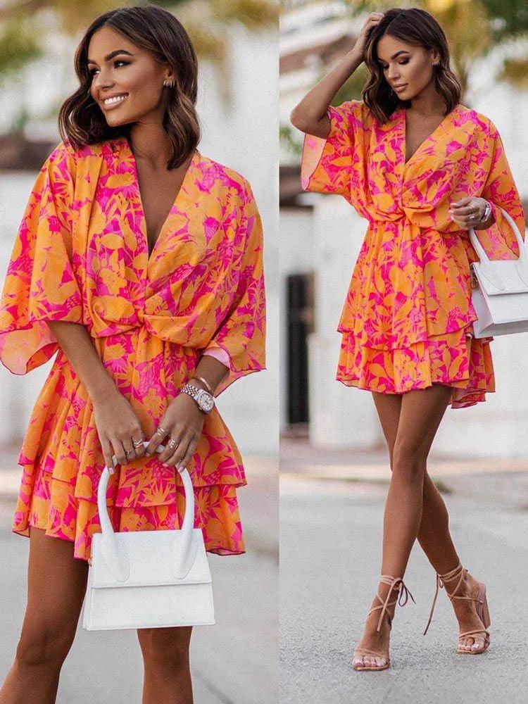 Donna con abito estivo floreale rosa e arancione, maniche ampie, borsa bianca e sandali con tacco. Moda femminile elegante e colorata.