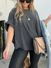 Donna con maglietta oversize nera con borchie, leggings neri, borsa a tracolla beige e occhiali da sole. Moda casual urbana.