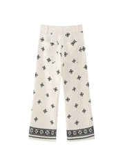 Pantaloni bianchi donna con motivo geometrico nero, taglio ampio, tasche posteriori, orlo decorato. Stile casual elegante.