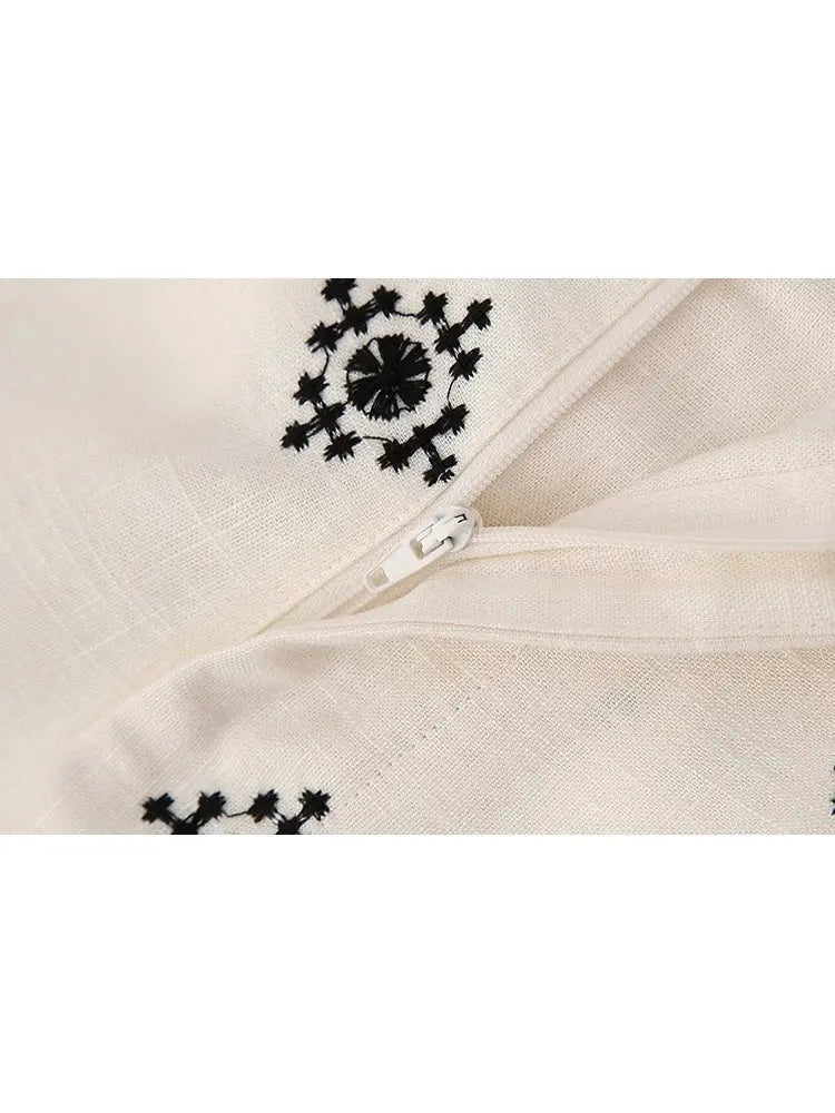 Cerniera bianca su tessuto beige con ricami neri geometrici. Dettaglio moda, abbigliamento elegante, design tessile artigianale.