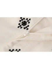 Cerniera bianca su tessuto beige con ricami neri geometrici. Dettaglio moda, abbigliamento elegante, design tessile artigianale.