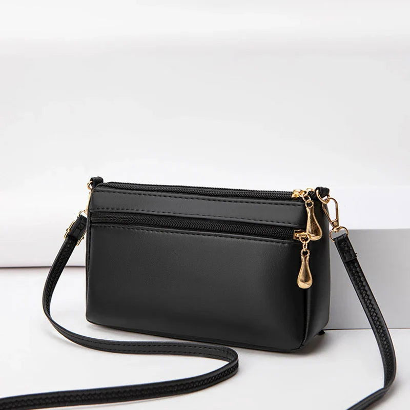 Borsa a tracolla nera in pelle sintetica con cerniere dorate, design elegante e compatto, ideale per moda donna e accessori quotidiani.