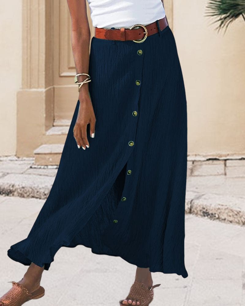 Gonna lunga blu scuro con bottoni, cintura marrone, indossata con sandali e top bianco. Moda estiva donna, abbigliamento casual elegante.