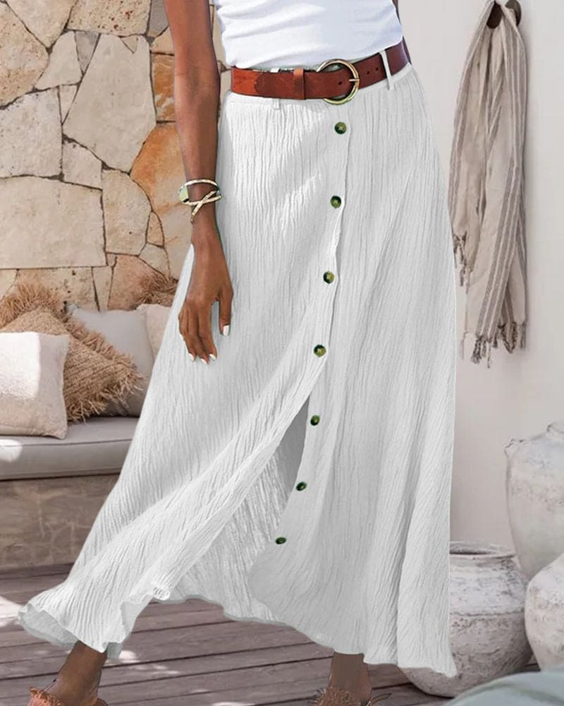 Gonna lunga bianca a pieghe con bottoni verdi, cintura marrone, indossata da una donna. Moda estiva, abbigliamento casual elegante.