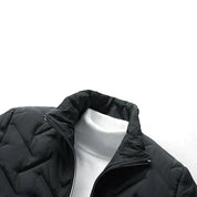 Giacca nera trapuntata da uomo con collo alto, indossata sopra un maglione bianco a collo alto. Moda invernale elegante e calda.
