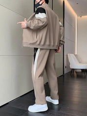 Uomo in tuta sportiva beige e bianca, scarpe da ginnastica bianche, posa moderna. Abbigliamento casual, moda uomo, stile urbano.
