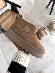 Stivaletto beige in pelle scamosciata con suola spessa, design moderno e minimalista, perfetto per l'inverno. Arredamento elegante sullo sfondo.