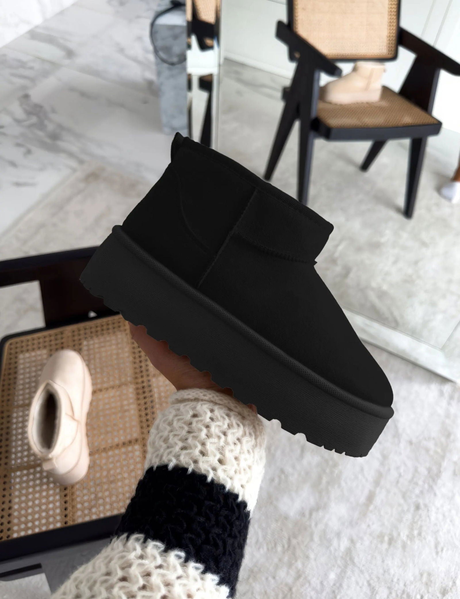 Scarpa invernale nera suola spessa, design moderno, tenuta in mano, sfondo interno con sedia e specchio. Calzature moda, comfort, stile casual.