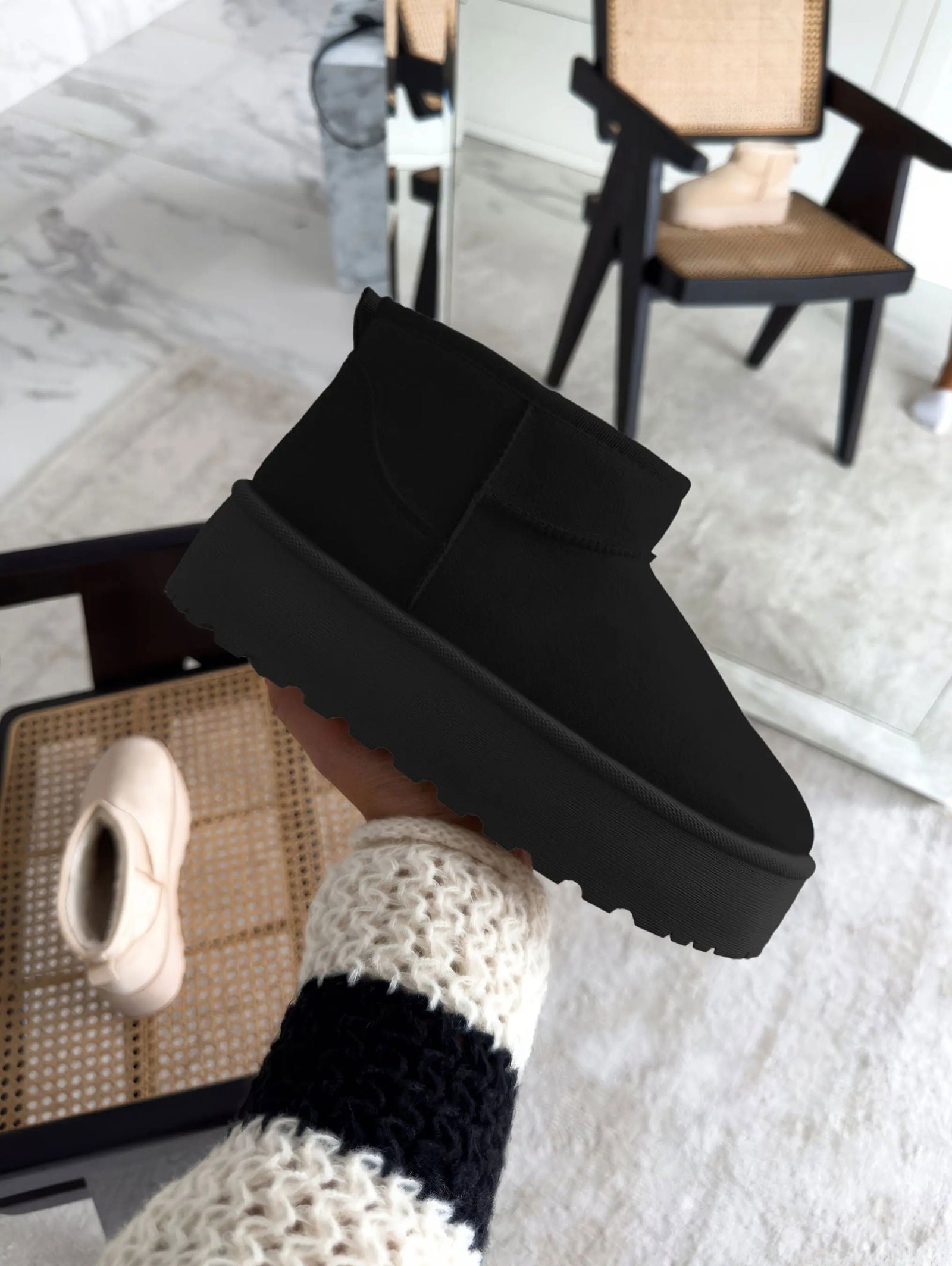 Scarpa invernale nera suola spessa, design moderno, tenuta in mano, sfondo interno con sedia e specchio. Calzature moda, comfort, stile casual.
