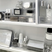 Organizzatore trasparente per cosmetici su scaffale bianco, contenente profumi, creme, sieri e trucchi. Soluzione elegante per l'archiviazione del trucco.