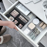 Cassetto aperto con trucchi organizzati: palette ombretti, pennelli trucco, cipria e specchio. Organizzazione cosmetici bagno moderno.