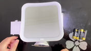 Specchio cosmetico quadrato con luce LED, supporto regolabile e vano batterie, su sfondo nero. Include pile AA e decorazione a forma di fiore.
