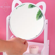 Specchio da tavolo girevole a 360°, design orecchie di gatto, colore bianco, con foglie tropicali riflettenti, su sfondo rosa. Accessorio decorativo.