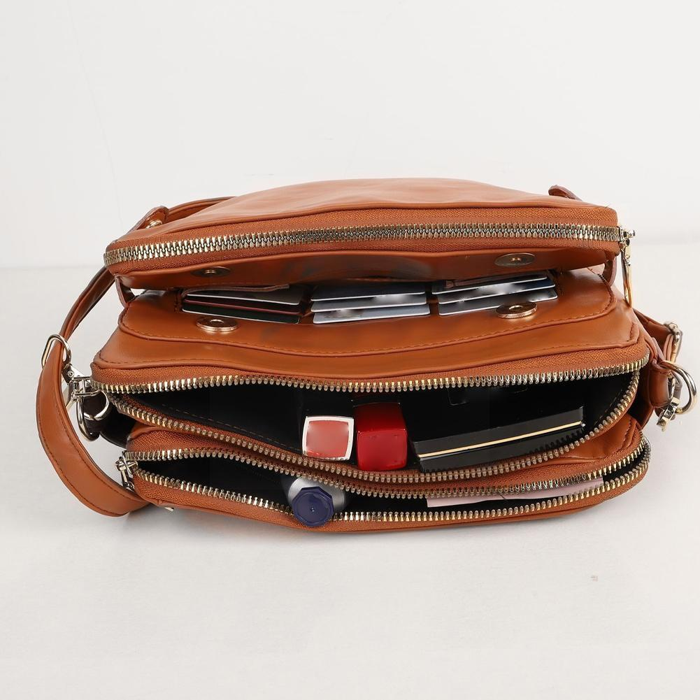 Borsa a tracolla in pelle marrone con zip aperte, mostra scomparti interni contenenti rossetto, smartphone e portafoglio. Accessorio moda elegante.