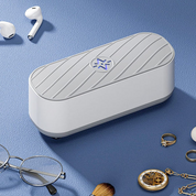 Sterilizzatore UV portatile bianco su tavolo blu, circondato da occhiali, anelli, orologio e auricolari. Dispositivo igienizzante per oggetti personali.
