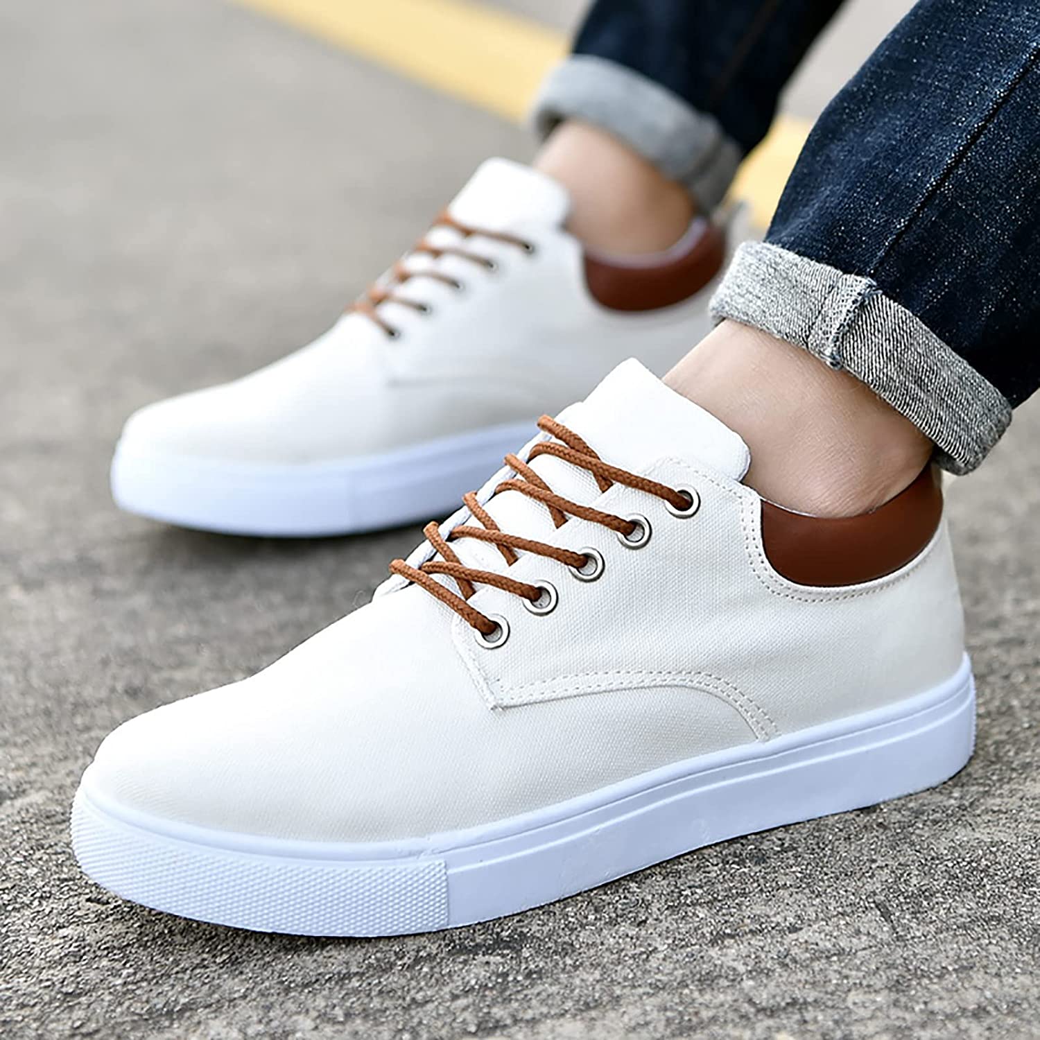Scarpe da ginnastica bianche da uomo, suola in gomma, lacci marroni, dettagli in pelle marrone, indossate con jeans. Sneakers casual eleganti.