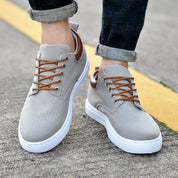 Scarpe da uomo casual grigie con lacci marroni, suola bianca, indossate su strada asfaltata. Scarpe eleganti e comode per uso quotidiano.