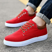 Scarpe da ginnastica rosse da uomo, suola bianca, lacci marroni, indossate su strada asfaltata. Design casual, moda urbana, comfort quotidiano.