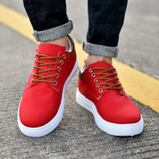Scarpe da ginnastica rosse unisex con lacci marroni, suola bianca, indossate su strada asfaltata. Moda casual, calzature comode, stile urbano.