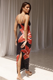 Abito lungo donna con spalline sottili, stampa floreale rossa su sfondo nero, spacco laterale, indossato da modella in ambiente elegante.